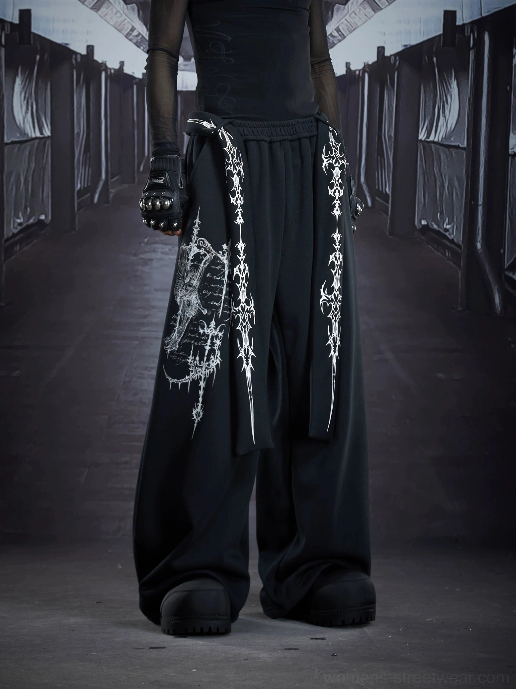 Black gothic streetwear cargo sweatpants detail view showing distressed sigil leg print, extra-wide drape, and cross strap accent