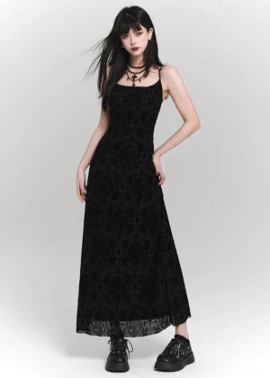 Full-body side view of a black gothic velvet maxi slip dress with cross print, spaghetti straps, flowing floor-length skirt, punk necklaces, and platform boots