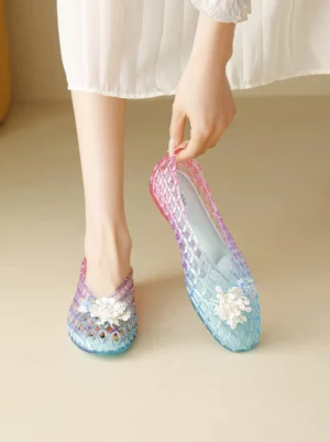 Woman wearing gradient jelly ballet flats with open grid texture and white flower toe accent styled with a white ruffled midi skirt
