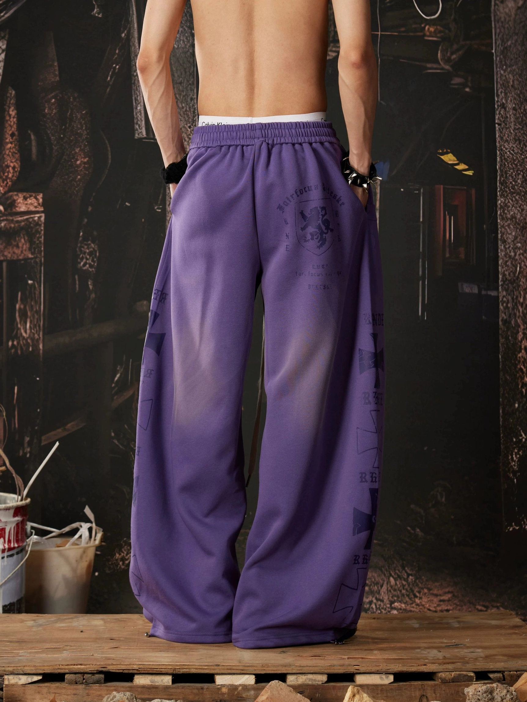 Gradient purple wide leg streetwear sweatpants shown from the rear with tonal graphic details, elastic waistband, and relaxed oversized silhouette