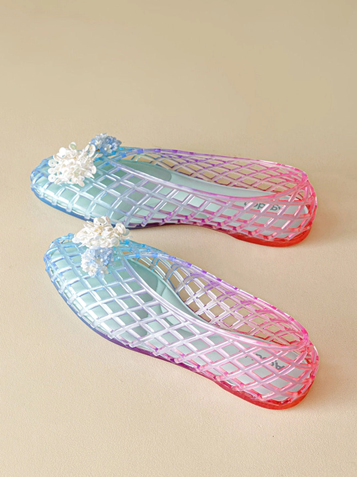 Top down product view of matching gradient rainbow jelly ballet flats with cyan to rose ombre and white flower accents
