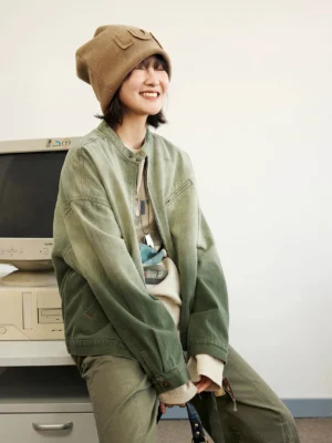 Green gradient washed denim flight jacket worn by female model in seated three-quarter front view
