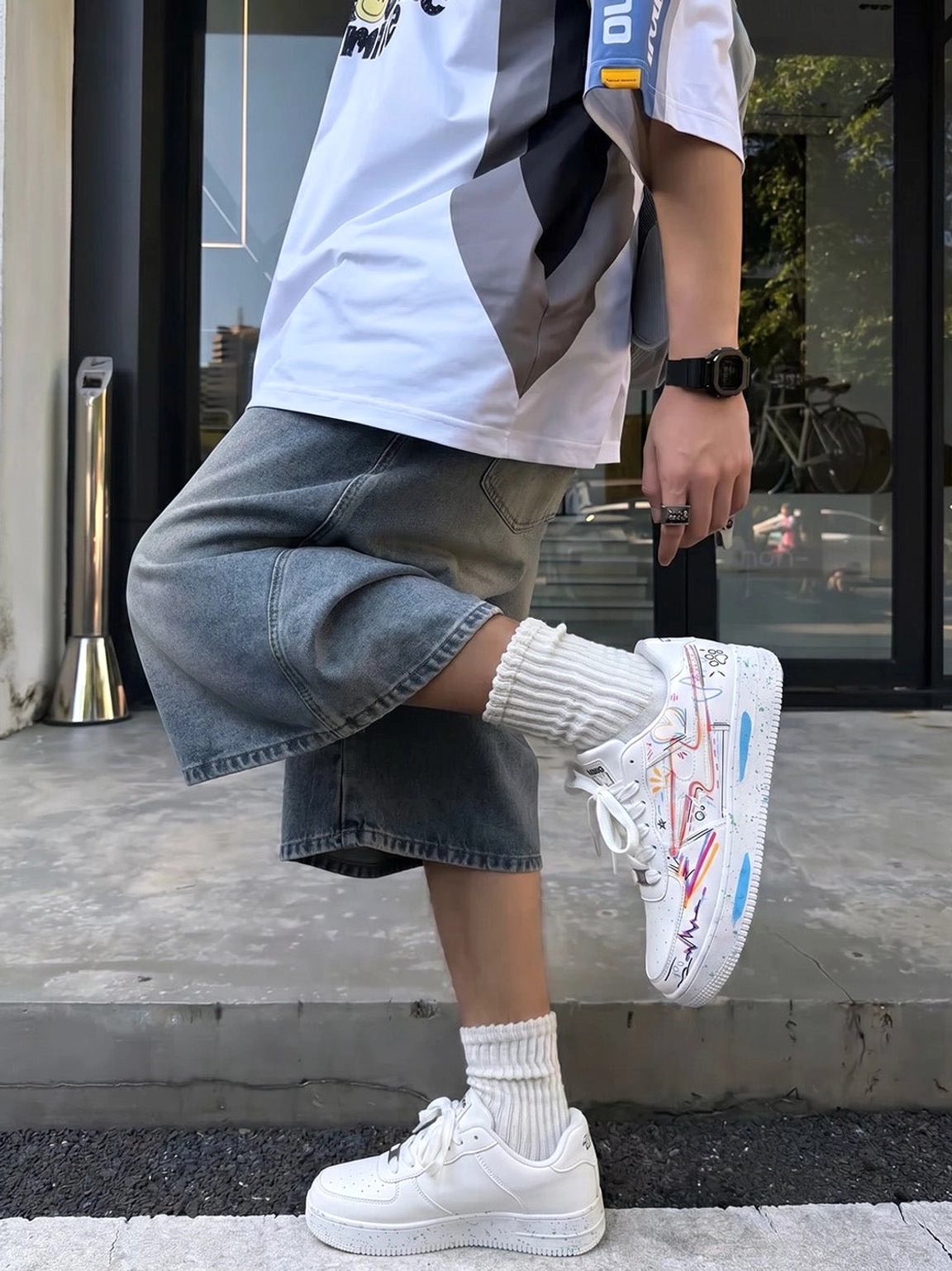 Graffiti print low-top court sneakers worn with denim shorts and white crew socks outside a streetwear shop entrance