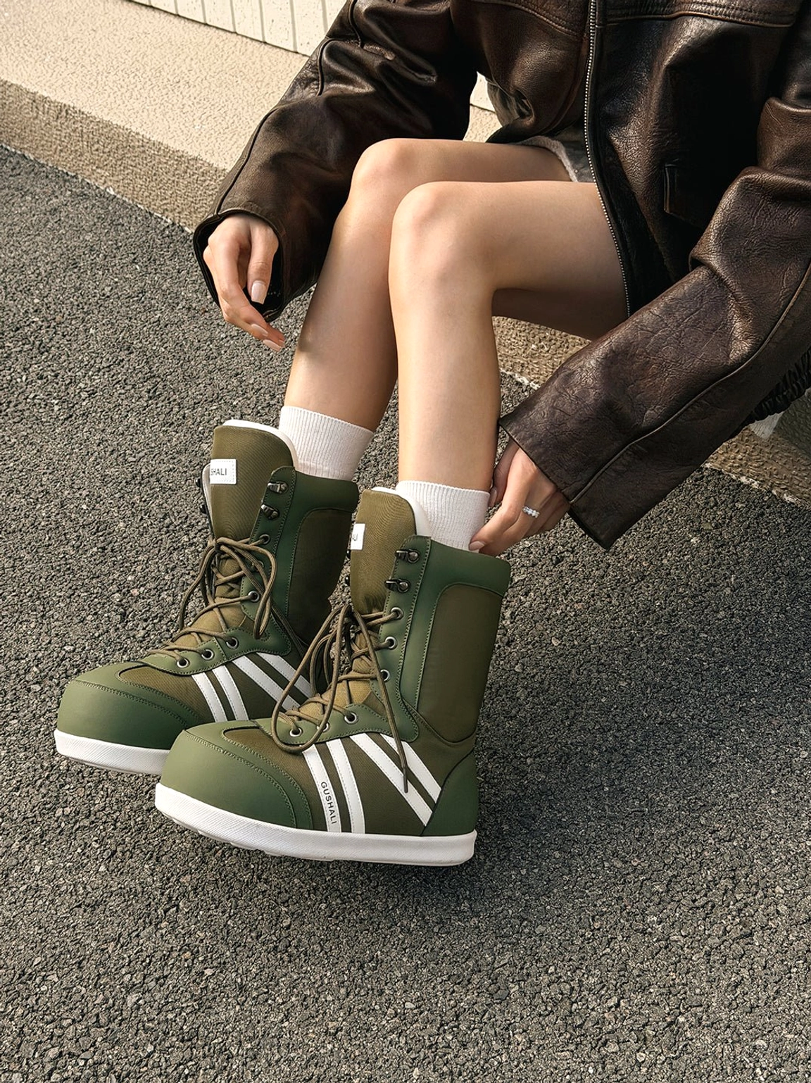 Olive green graphic lace-up snow boots with white stripe accents styled outdoors with crew socks