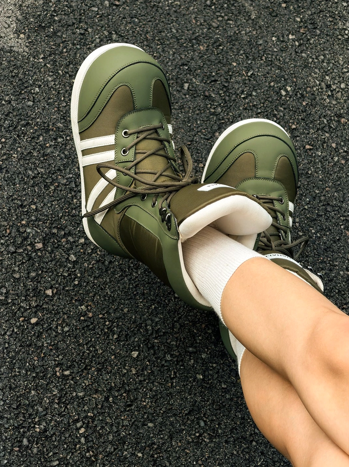 Top-down view of olive green fleece-lined graphic lace-up snow boots with contrast stripes on pavement