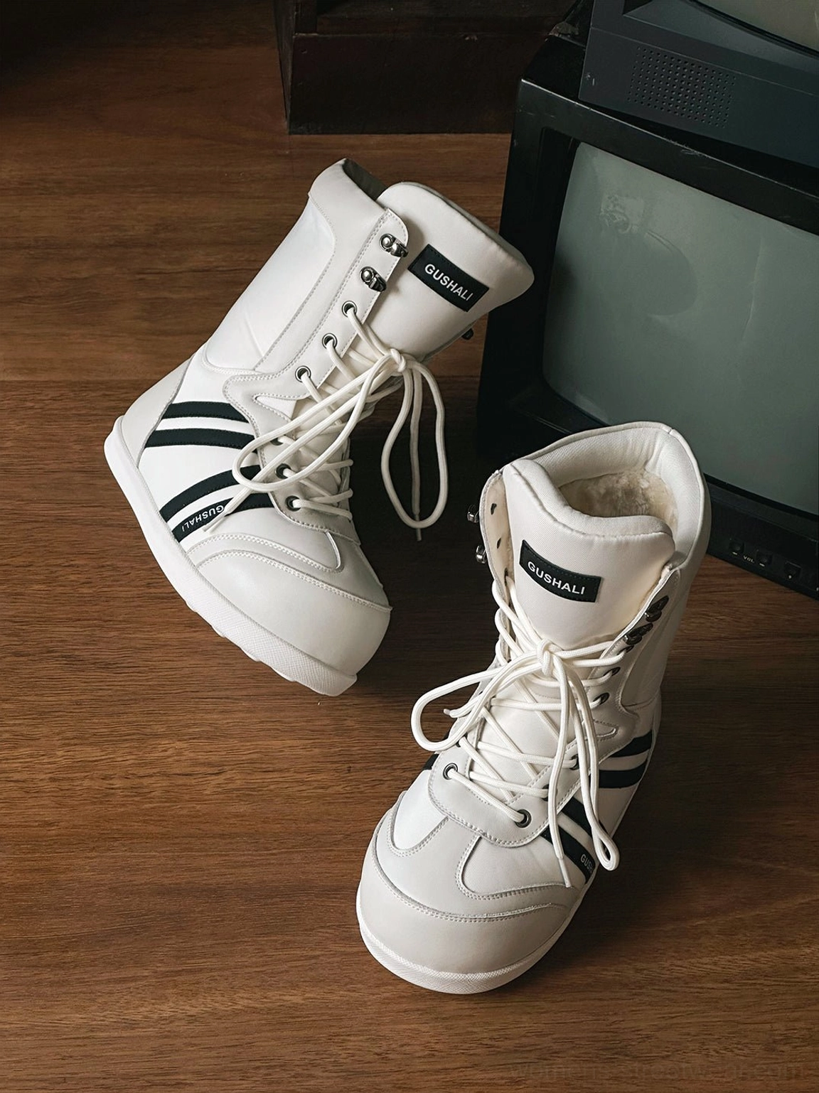 White fleece-lined graphic lace-up snow boots with black contrast stripe details displayed on a wooden table