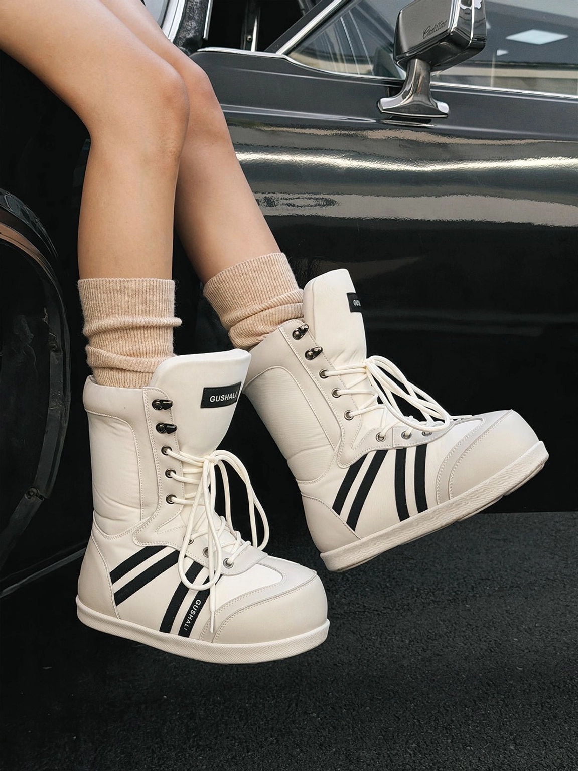 White graphic lace-up mid-calf snow boots with black stripes worn beside a vintage black car