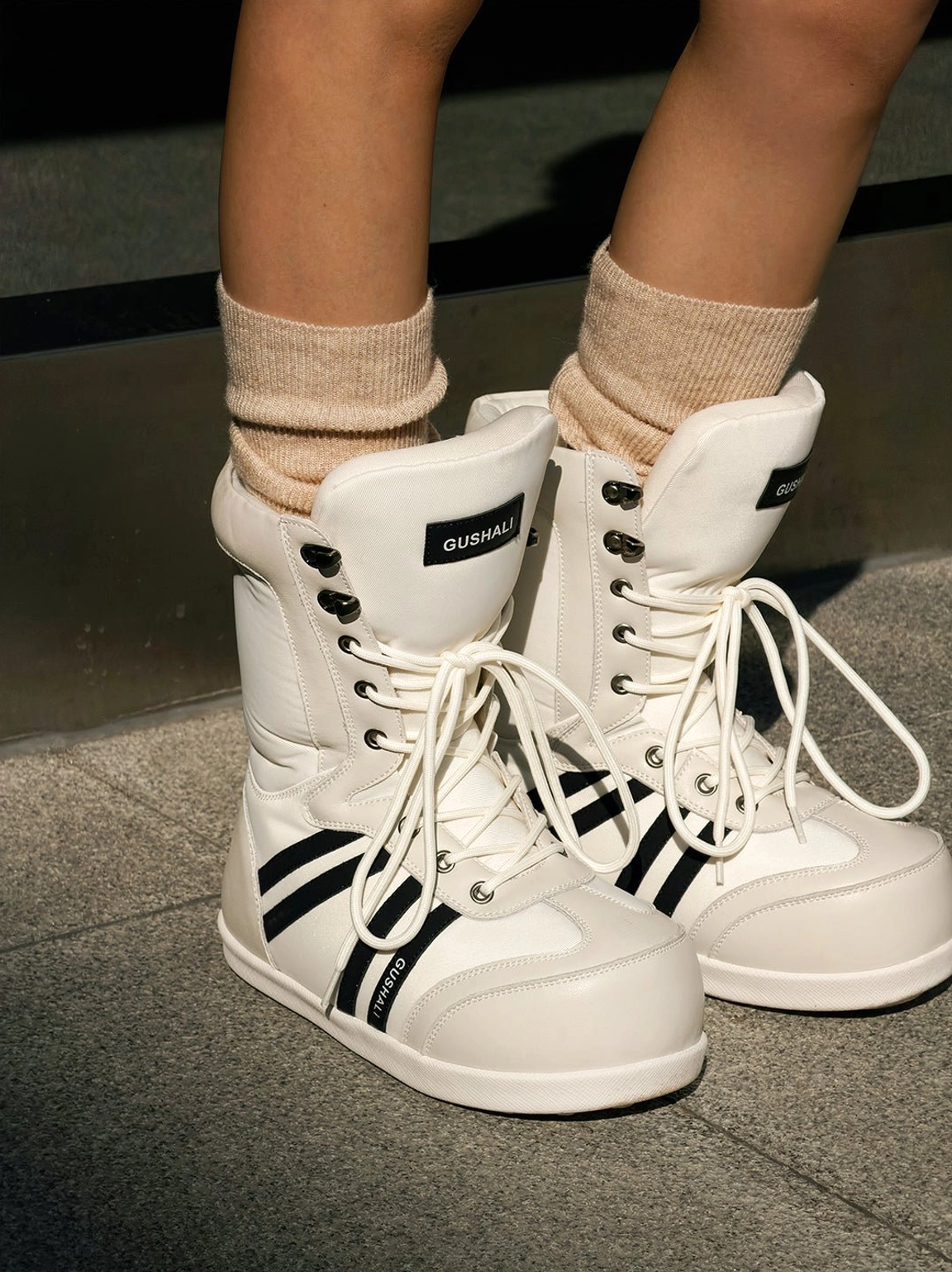 Close-up top view of white graphic fleece-lined lace-up snow boots styled with beige crew socks