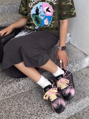 Female model wearing graphic pink-trim chunky sneakers with a camouflage top and midi skirt on concrete stairs
