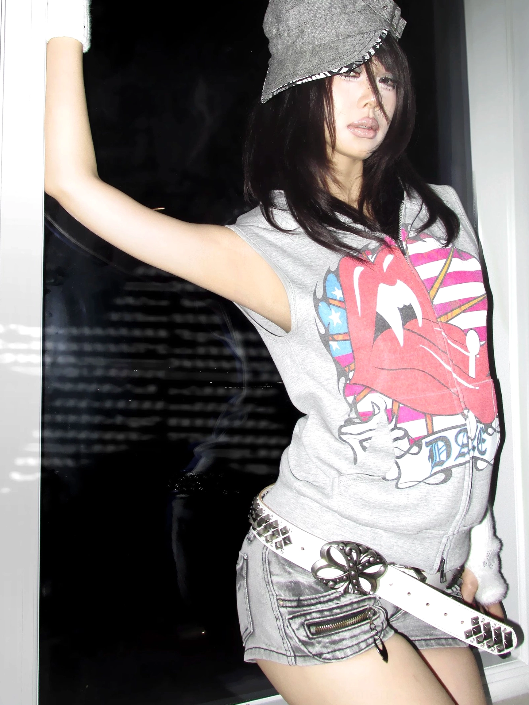 Side view of female model styling a gray sleeveless hooded vest with bold red lips and American flag graphic