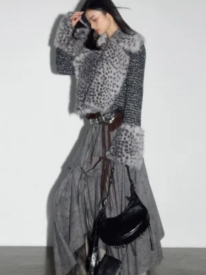 Model wearing a gray asymmetrical draped midi skirt with layered hem and cropped faux fur jacket in a minimalist streetwear studio