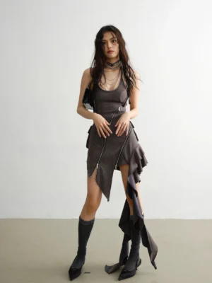 Front full-body view of a dark gray asymmetrical ruffled suspender dress with diagonal zipper, halter neckline, layered necklaces, and dark heeled boots