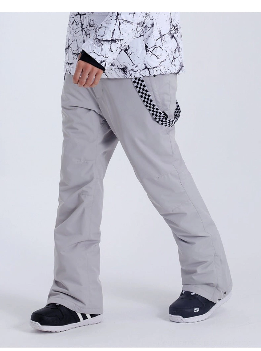 Model wearing light gray detachable snow pants with checkerboard suspenders and a printed ski jacket in outdoor street style