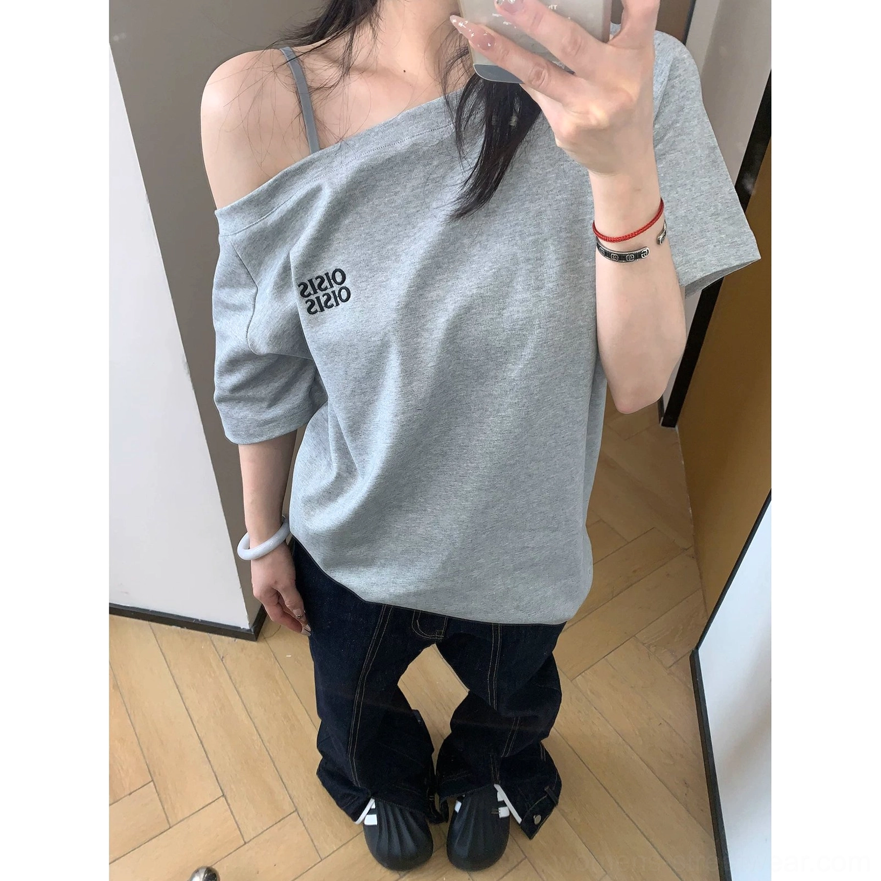 Close-up front view of soft gray cotton asymmetrical logo tee showing the exposed shoulder and layered spaghetti strap