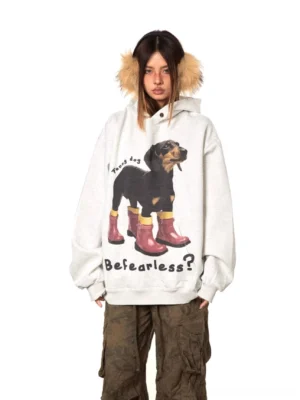 Gray oversized dog graphic hoodie with dachshund wearing red rain boots, fearless slogan, and soft hood trim shown in a front three-quarter streetwear outfit