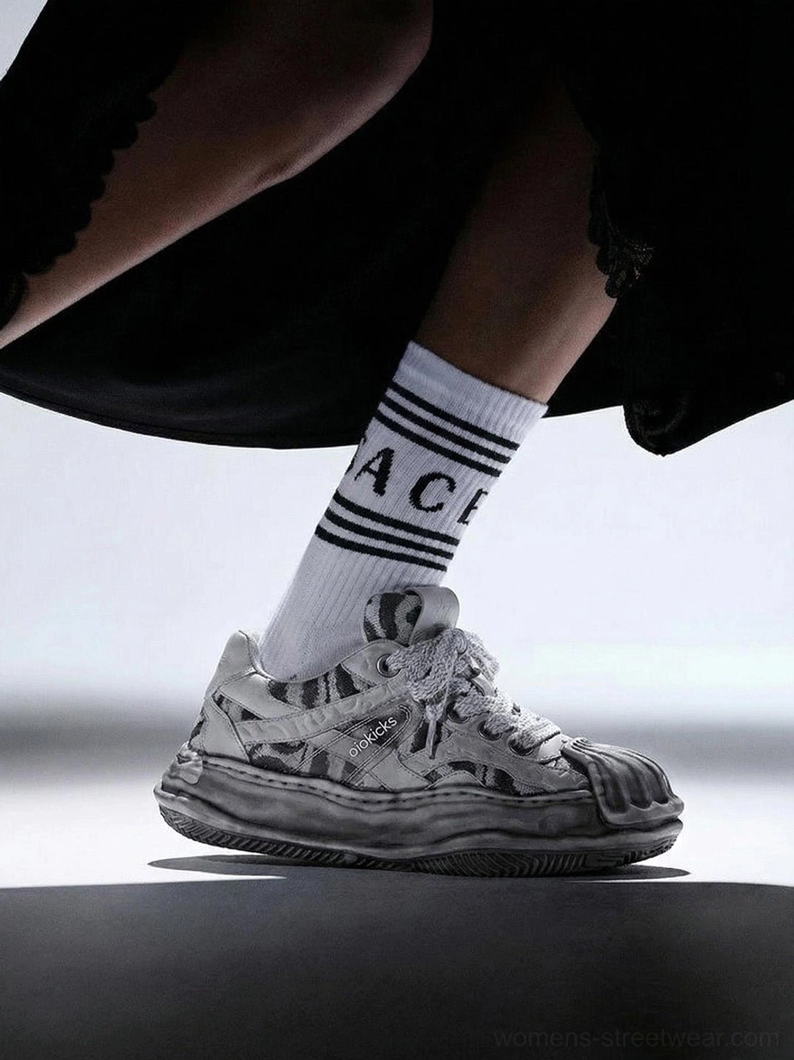 Gray distressed camo shell-toe skate sneaker styled with letter-print mid-calf socks and a black skirt in a side rear streetwear view