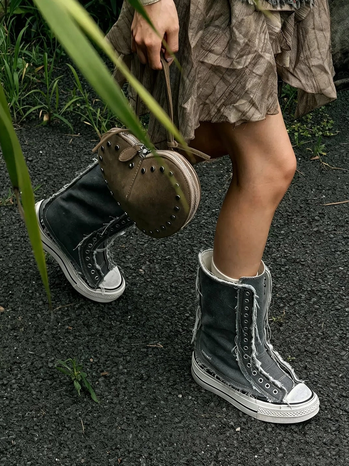 Woman styling dark gray distressed canvas platform boots with a ruffled brown midi skirt and handbag on an urban street