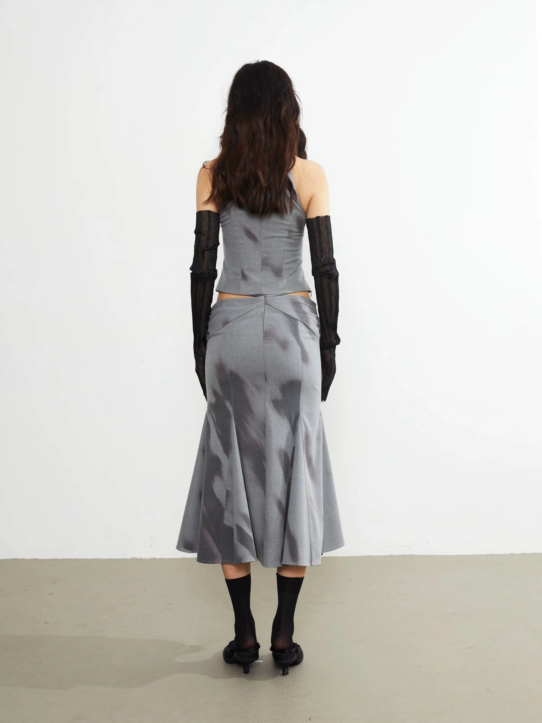 Back view of a gray embellished fishtail midi skirt with exposed waist styling, abstract print, and fluid flared hem