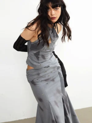 Close-up side view of a gray embellished midi skirt with twisted waist detail, cutout styling, and fluid flared fishtail hem
