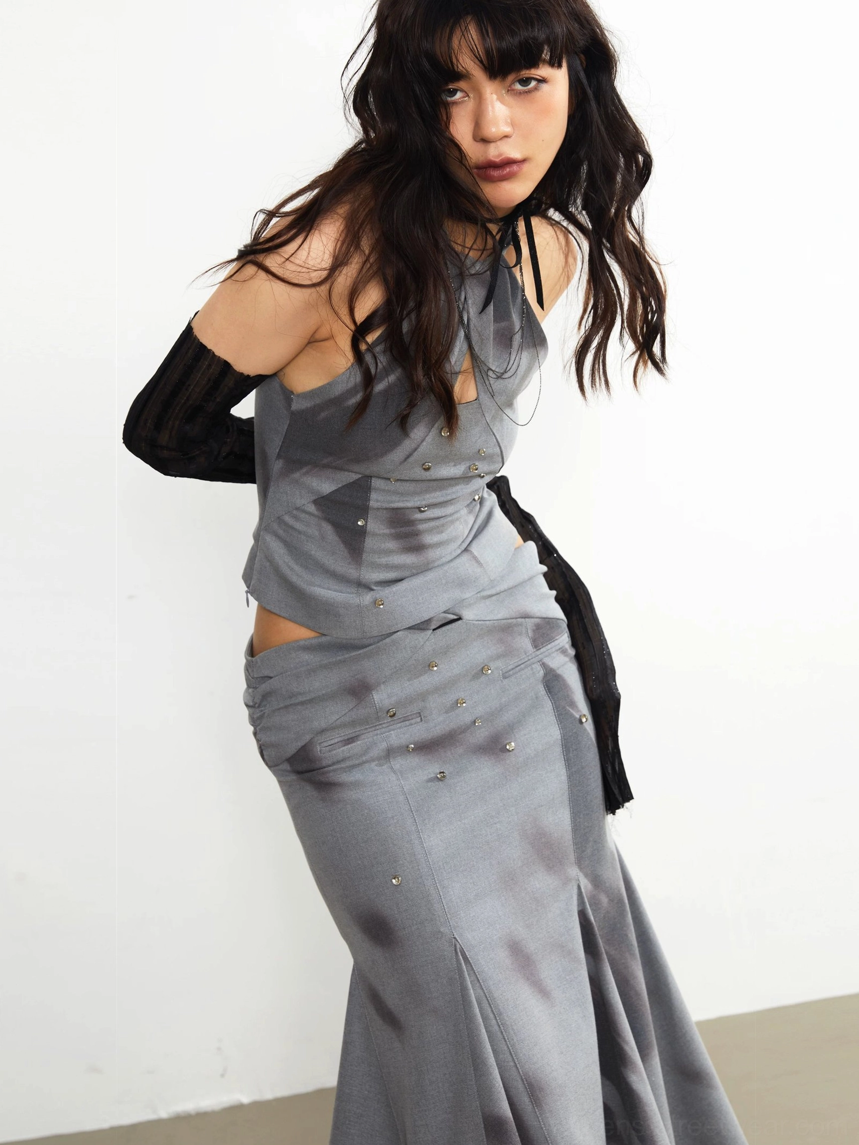 Close-up side view of a gray embellished midi skirt with twisted waist detail, cutout styling, and fluid flared fishtail hem