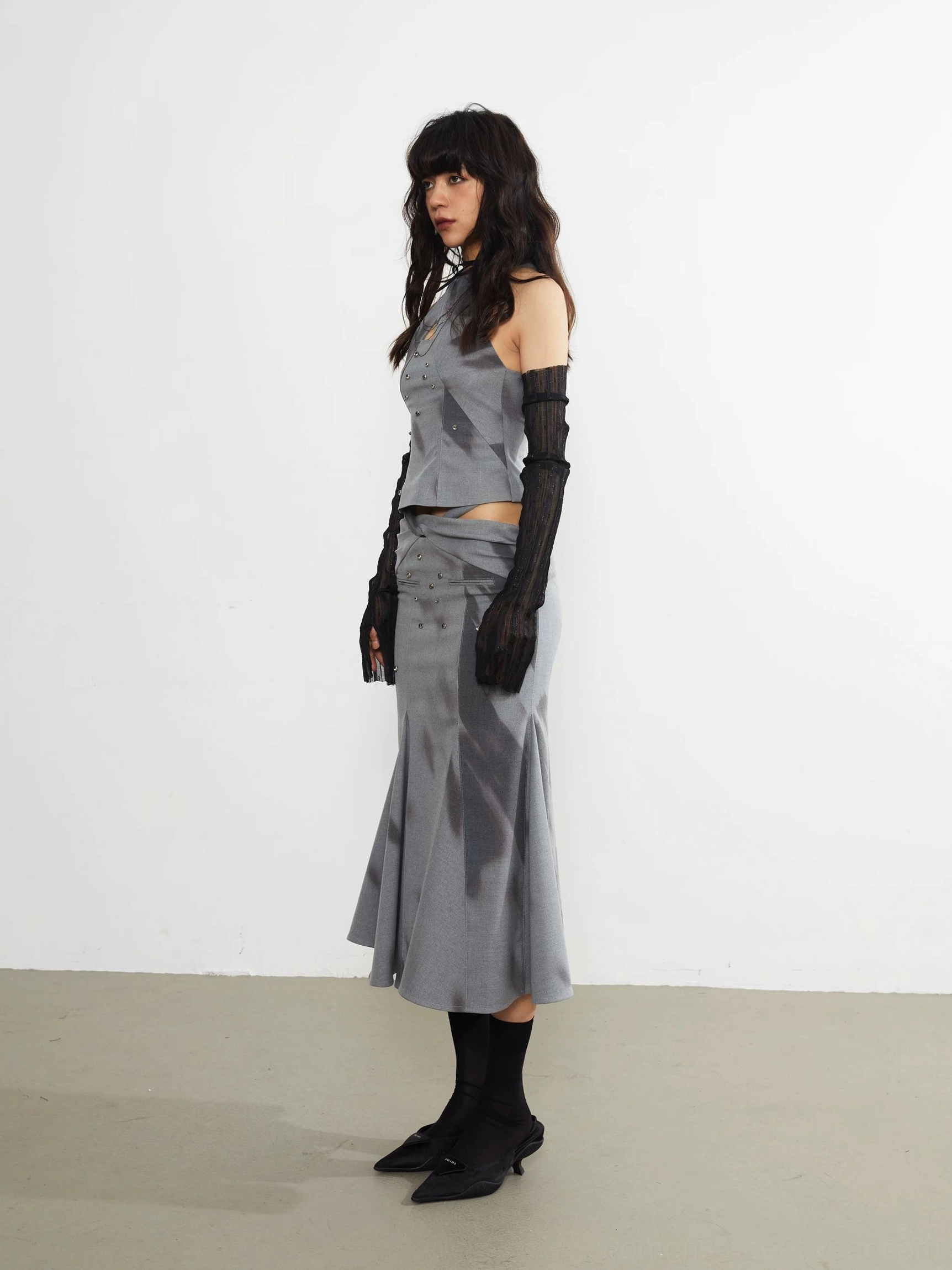 Side profile of a gray fitted fishtail midi skirt with abstract print, sculpted waist, and flowing mid-calf hem