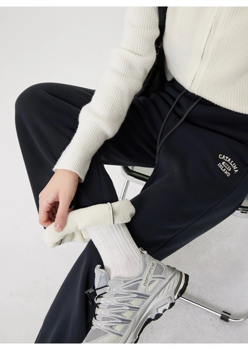 Side detail of gray fleece-lined streetwear sweatpants being adjusted at the cuff, revealing the soft lining and embroidered upper-thigh detail