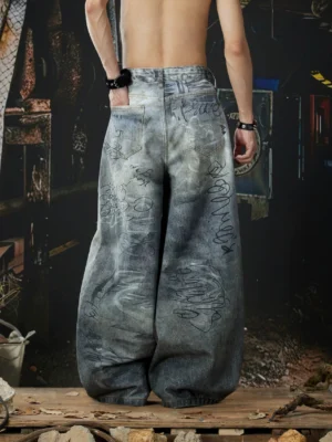 Rear view of faded gray graffiti wide-leg jeans showing printed back pockets, graphic denim artwork, relaxed hip fit, and extra-wide stacked trouser legs