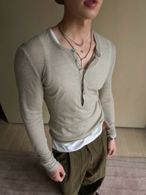 Close-up of gray green ribbed deep V Henley long sleeve streetwear top layered over a white undershirt with necklaces