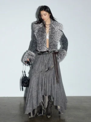 Front three-quarter view of a gray high-waisted asymmetrical midi skirt with cutout waist styling, ankle boots, and shoulder bag