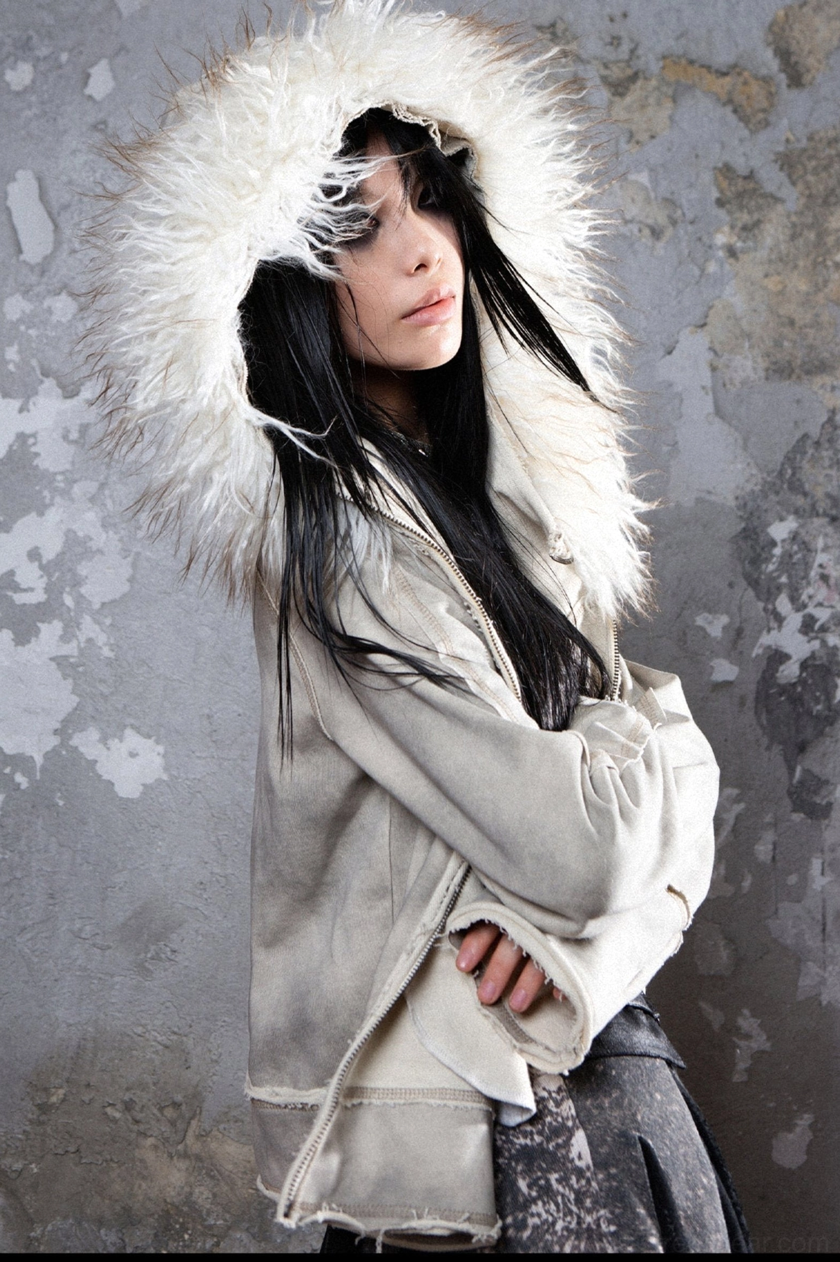 Gray hooded faux fur trim jacket side view styled with a dark patterned midi skirt and asymmetrical winter streetwear silhouette