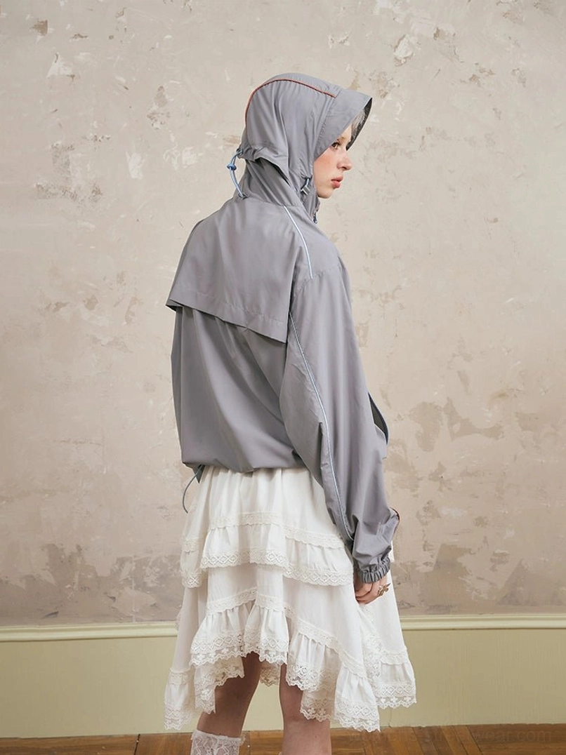 Back view of gray hooded windbreaker jacket and tiered lace midi skirt showing back yoke panel, contrast piping, and layered ruffle lace hem