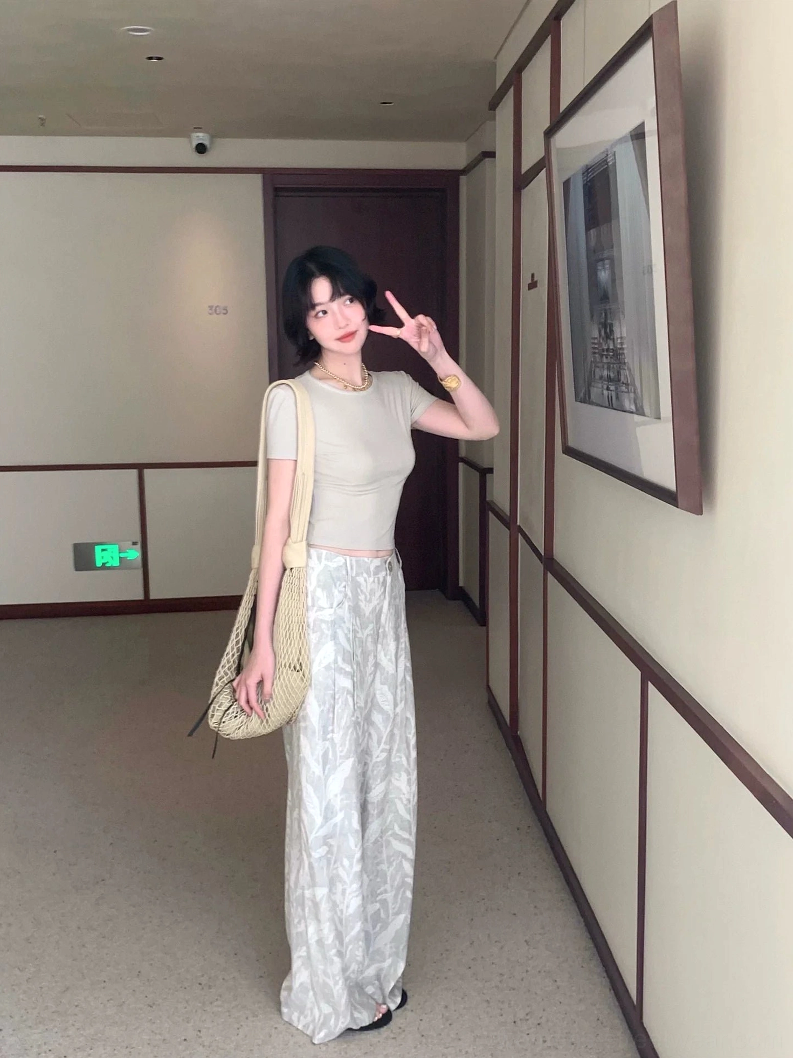 Full body view of gray leaf print high waisted pleated wide leg pants styled with a cropped top indoors