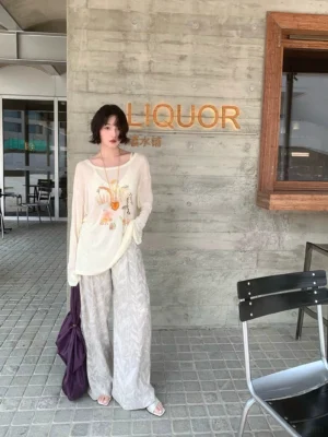 Gray leaf print wide leg pants styled with a loose printed long sleeve top and purple tote bag in an urban streetwear setting