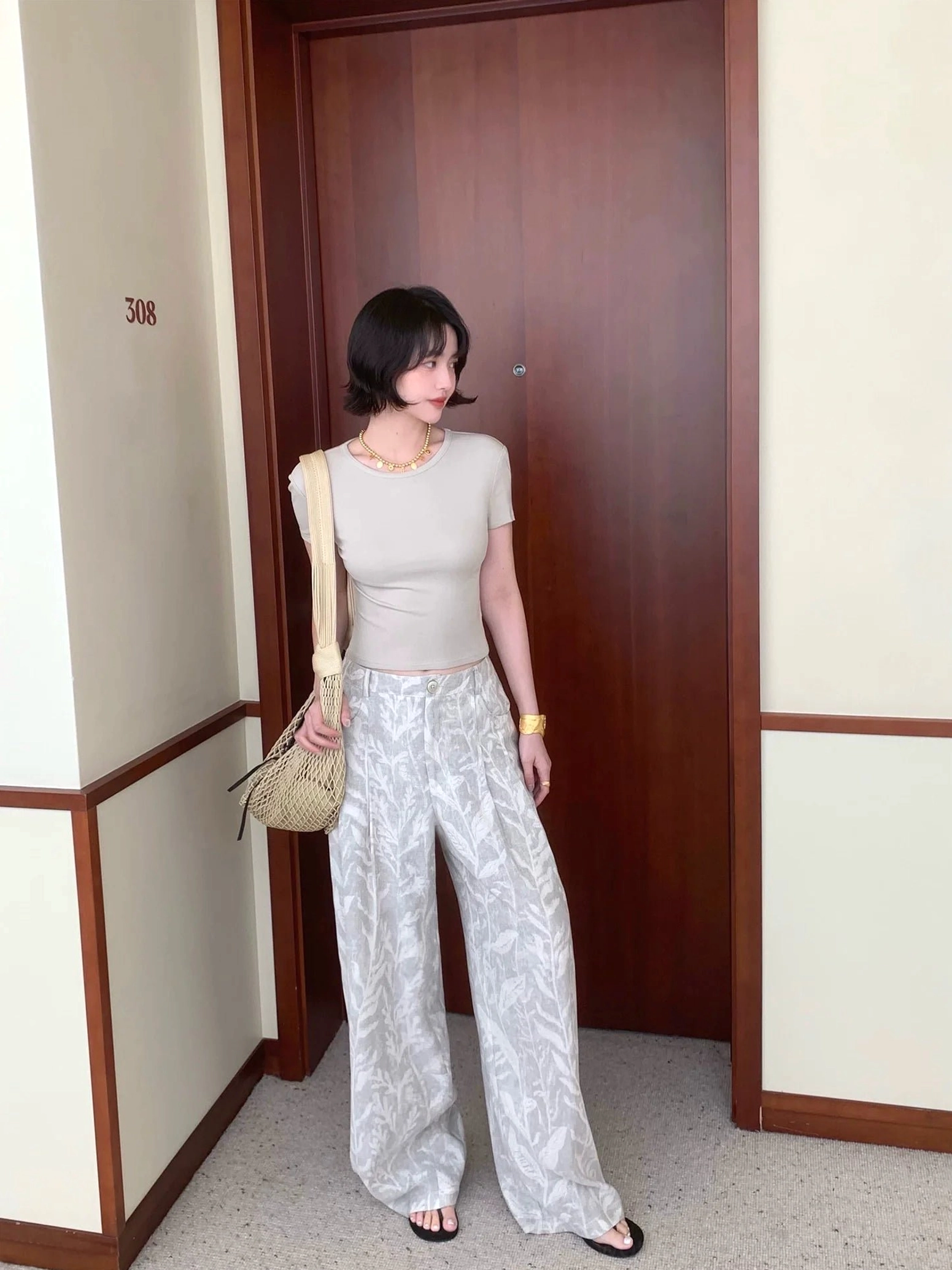 Gray leaf print wide leg streetwear pants styled with a cropped light gray top and woven shoulder bag in a hotel room