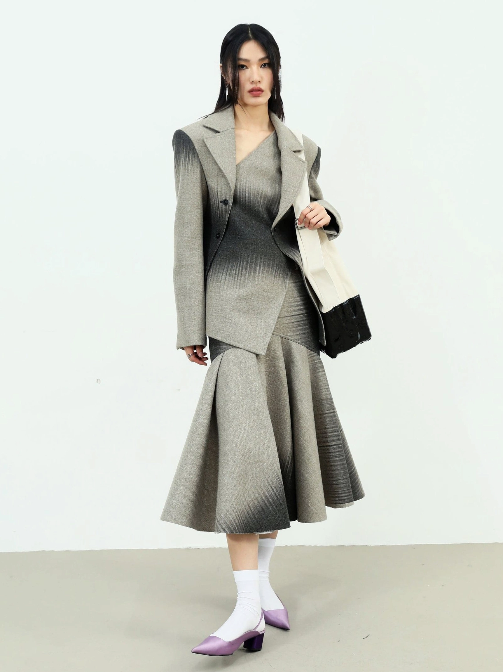 Front three-quarter view of a gray ombre fishtail maxi skirt with an asymmetrical blazer hem and structured streetwear styling