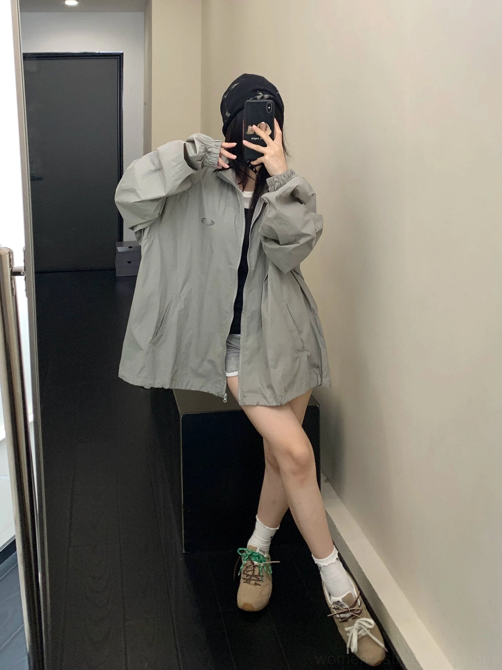 Side full-body view of a woman in an oversized gray Korean streetwear windbreaker with lantern sleeves, stand collar, baseball cap, shorts, socks, and sneakers