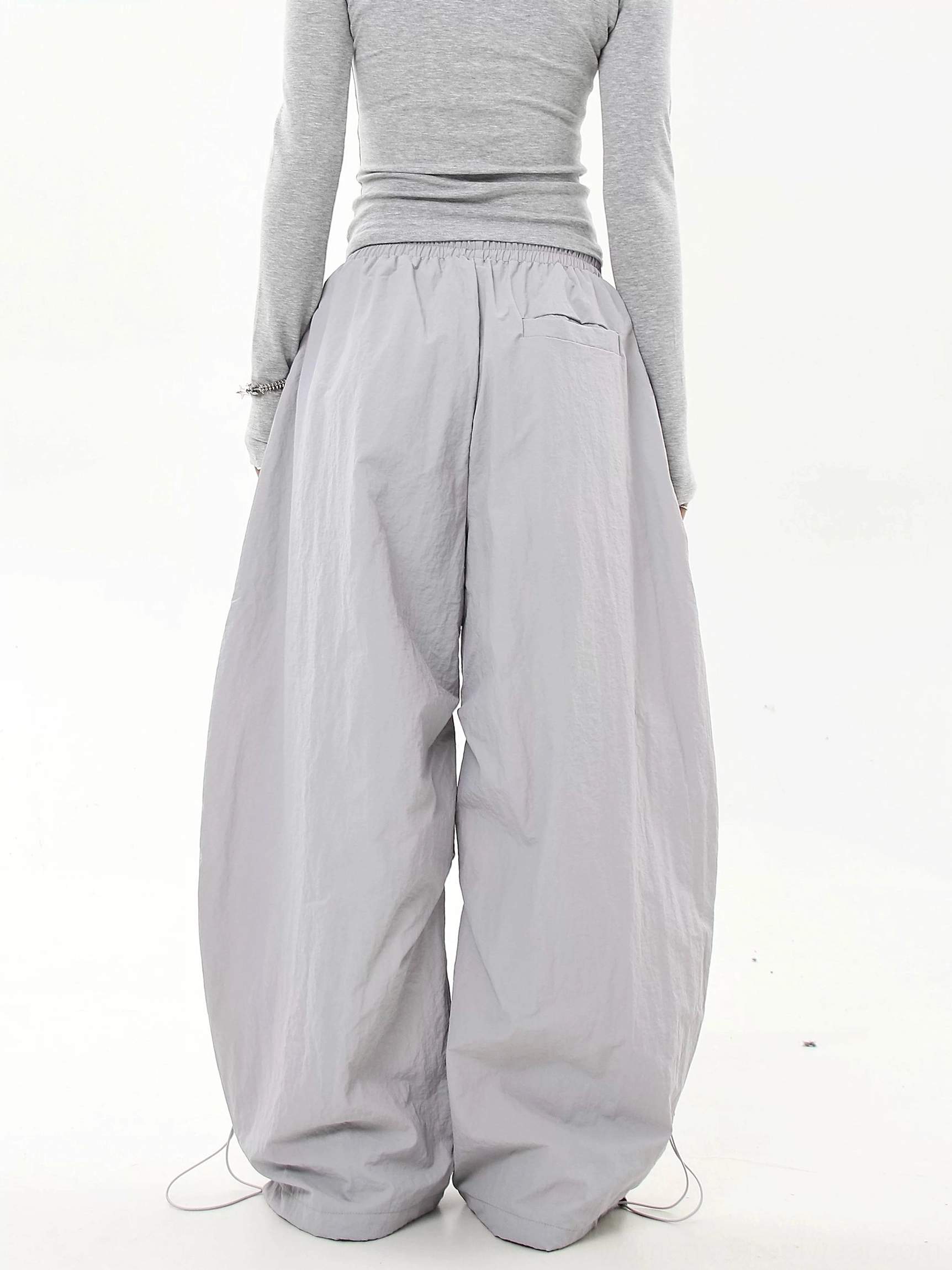 Back view of light gray oversized parachute streetwear cargo pants with a clean plain design, back pocket and adjustable drawstring cuffs