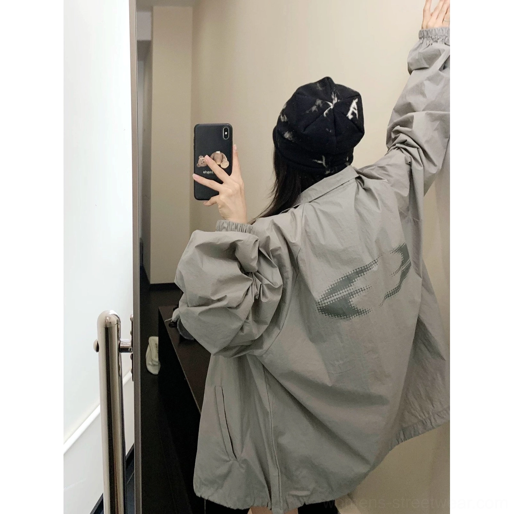 Back view of a woman wearing a gray oversized windbreaker jacket with understated back graphic, elastic cuffs, relaxed fit, and casual Korean streetwear styling