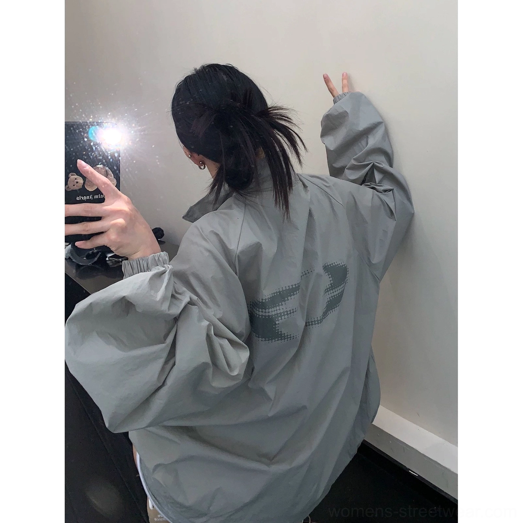 Back mirror view of an oversized gray windbreaker jacket showing subtle graphic detail, long loose sleeves, elastic cuffs, stand collar, and relaxed Seoul streetwear styling