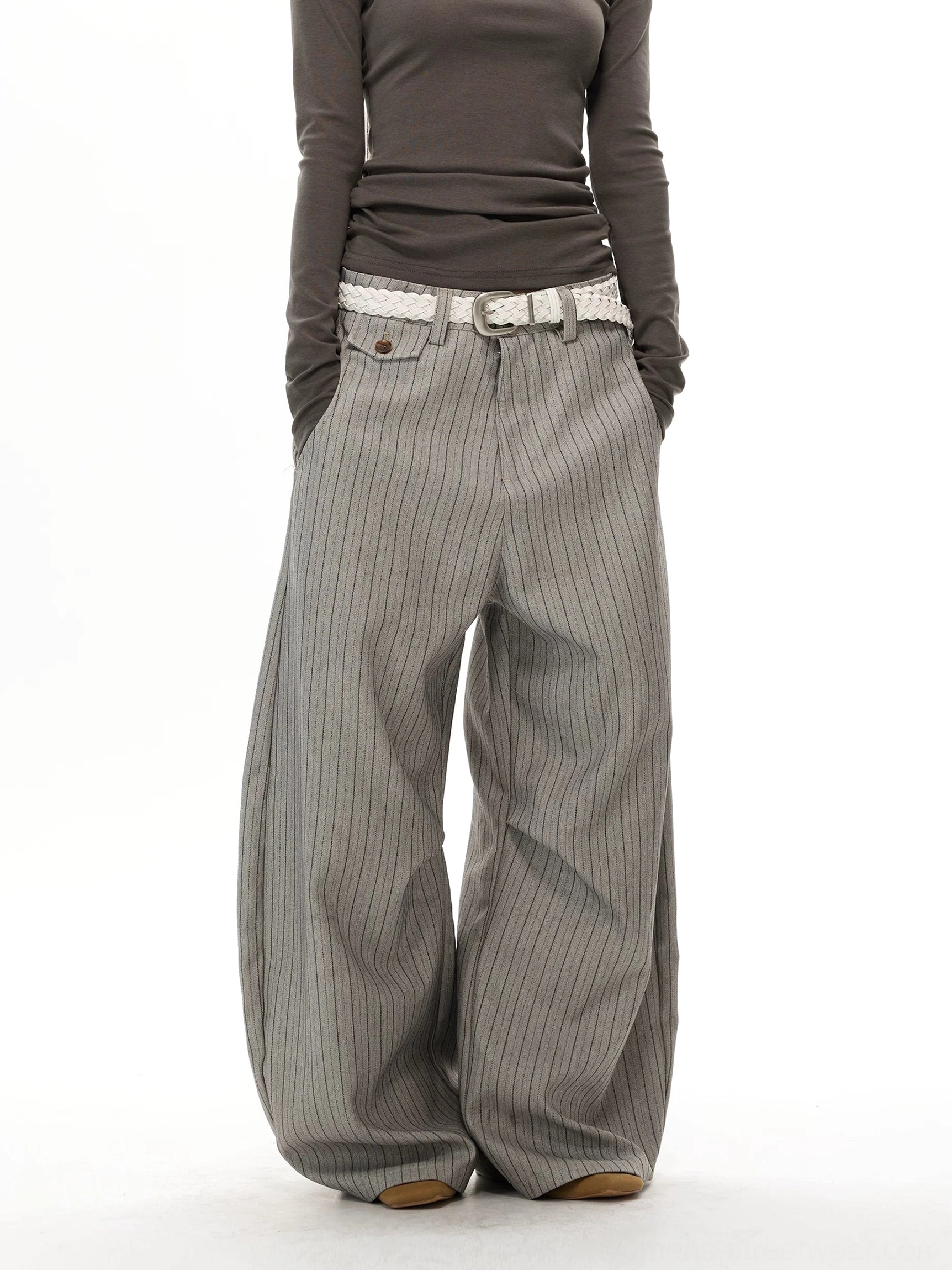 Close front detail of gray pinstripe streetwear trousers with slant pockets, belt loops, and tailored waistband