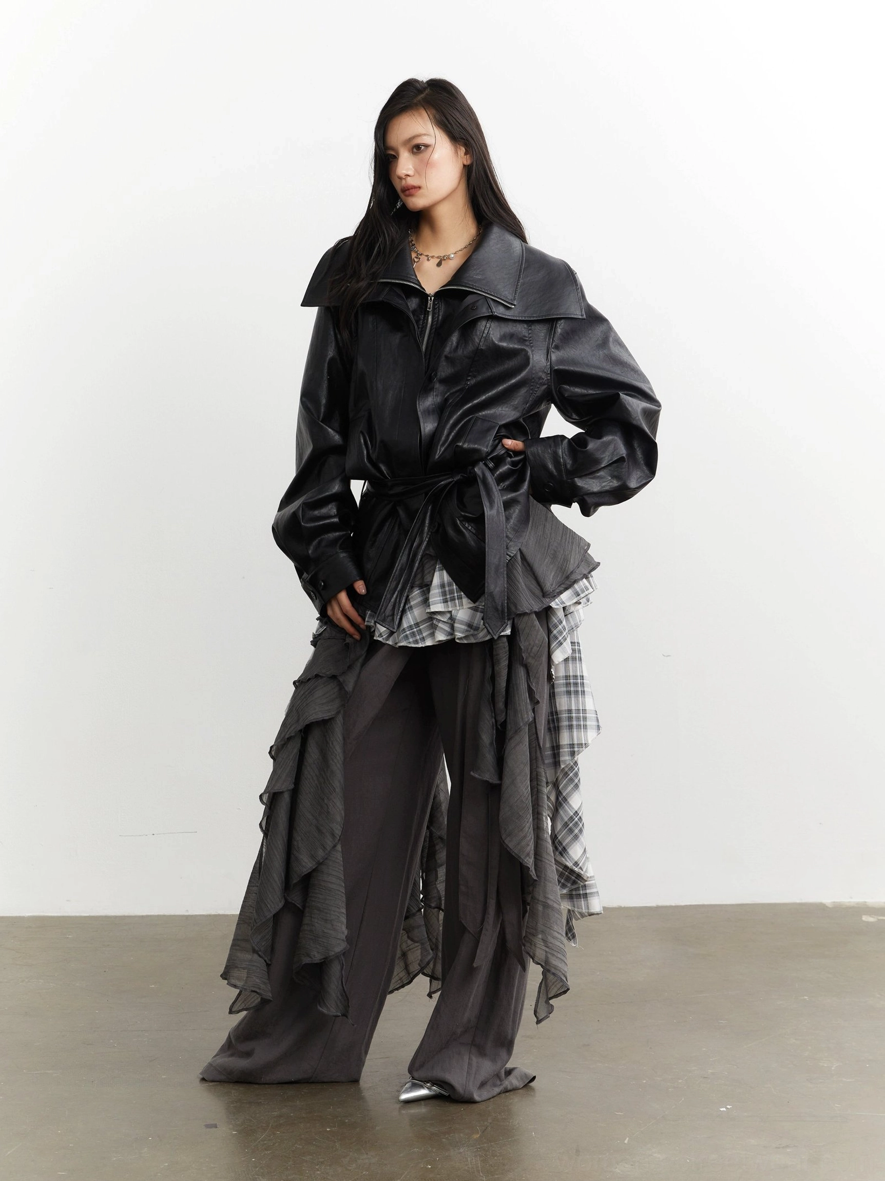 Side styled view featuring gray plaid ruffle deconstructed layering with black leather jacket and wide leg trousers