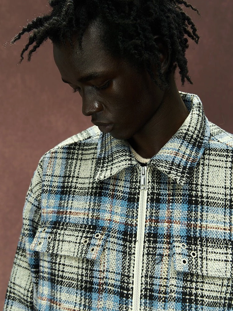 Close-up detail of textured woven gray plaid fabric, shirt collar, metal zipper, and buttoned chest pocket