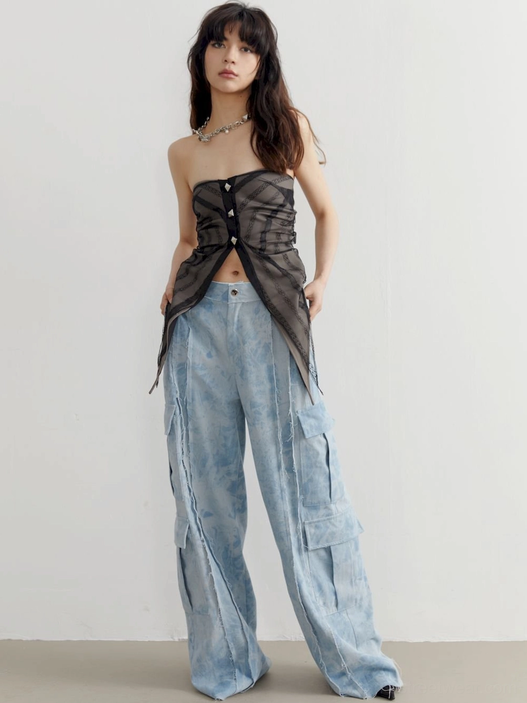 Front view of a gray sheer strapless tube top with pyramid studs, asymmetric hem, and acid-washed cargo denim