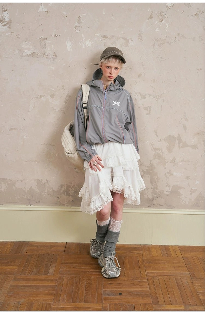 Front streetwear outfit featuring gray sporty hooded jacket, tiered lace midi skirt, bow embroidery, chunky sneakers, baseball cap, and crossbody bag
