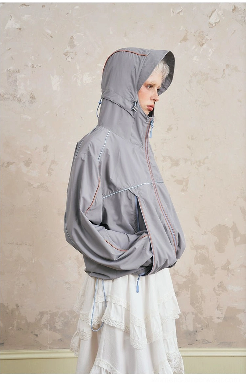 Side view of gray sporty hooded windbreaker jacket with drawstring hem, contrast piping, chest bow embroidery, side pockets, and lace midi skirt
