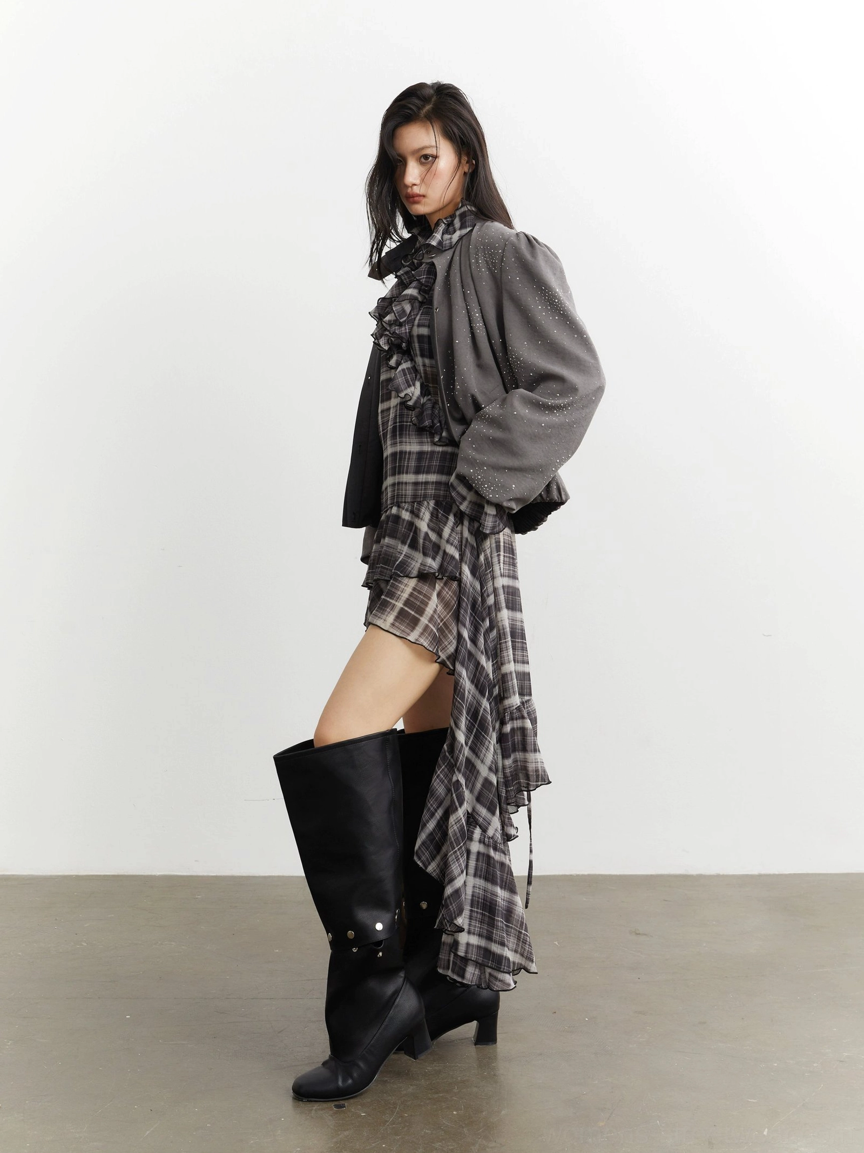 Side view of gray stardust cropped balloon sleeve streetwear jacket styled with a plaid ruffle dress and black over-the-knee boots