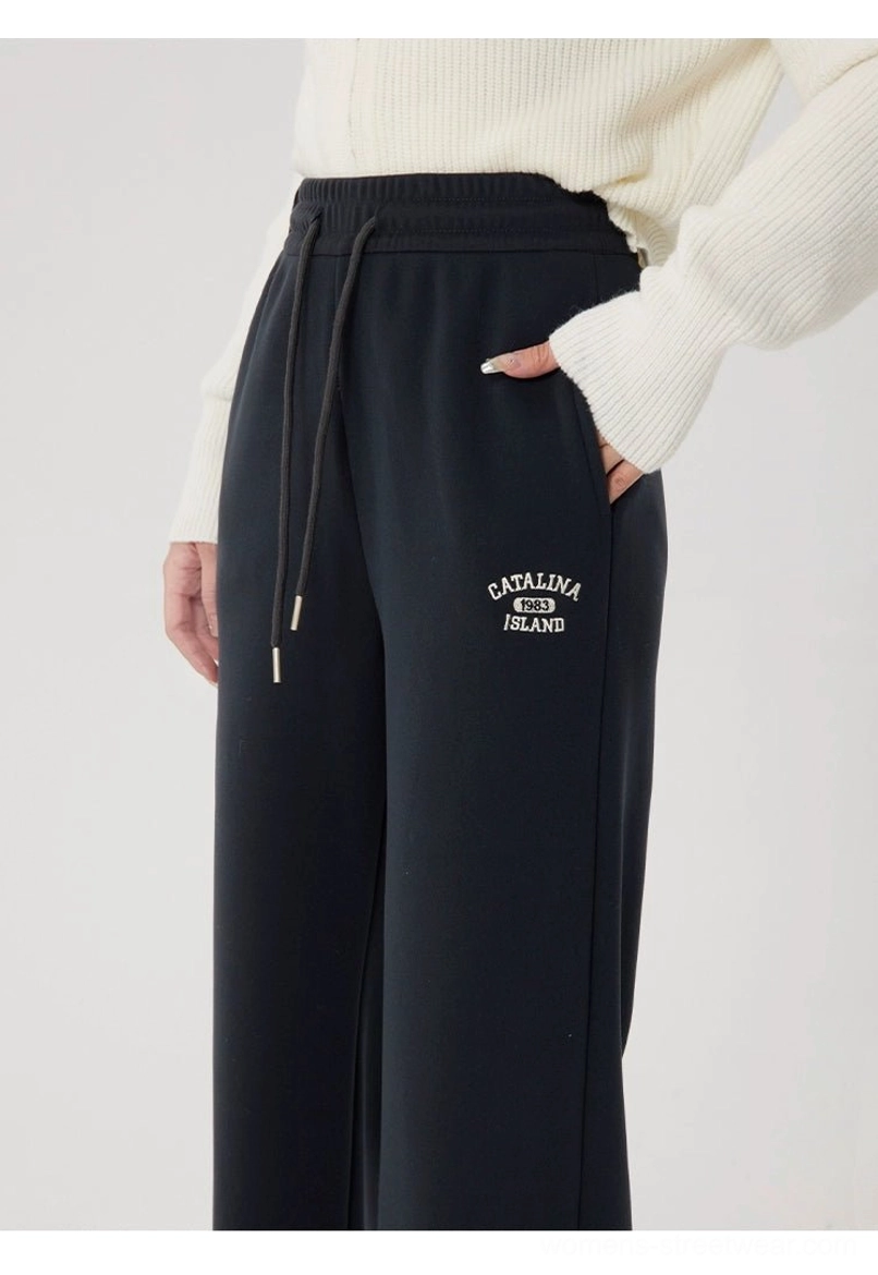 Side close-up of gray straight-leg fleece-lined sweatpants with a hand in the pocket, high-rise drawstring waist, and minimal embroidered detail