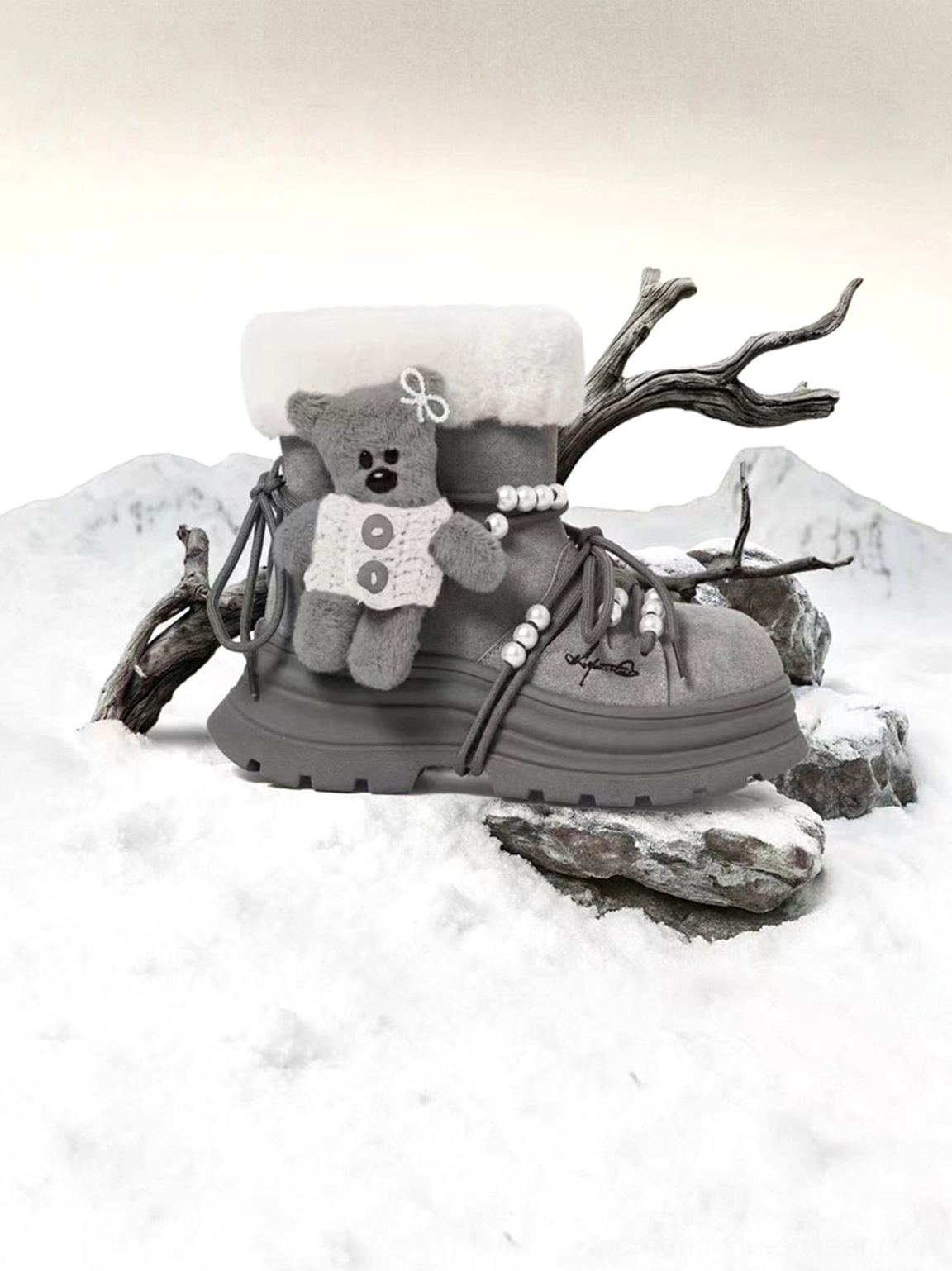 Gray teddy bear charm platform snow boot displayed on snowy rocks with plush collar pearl lace accents and winter mountain background