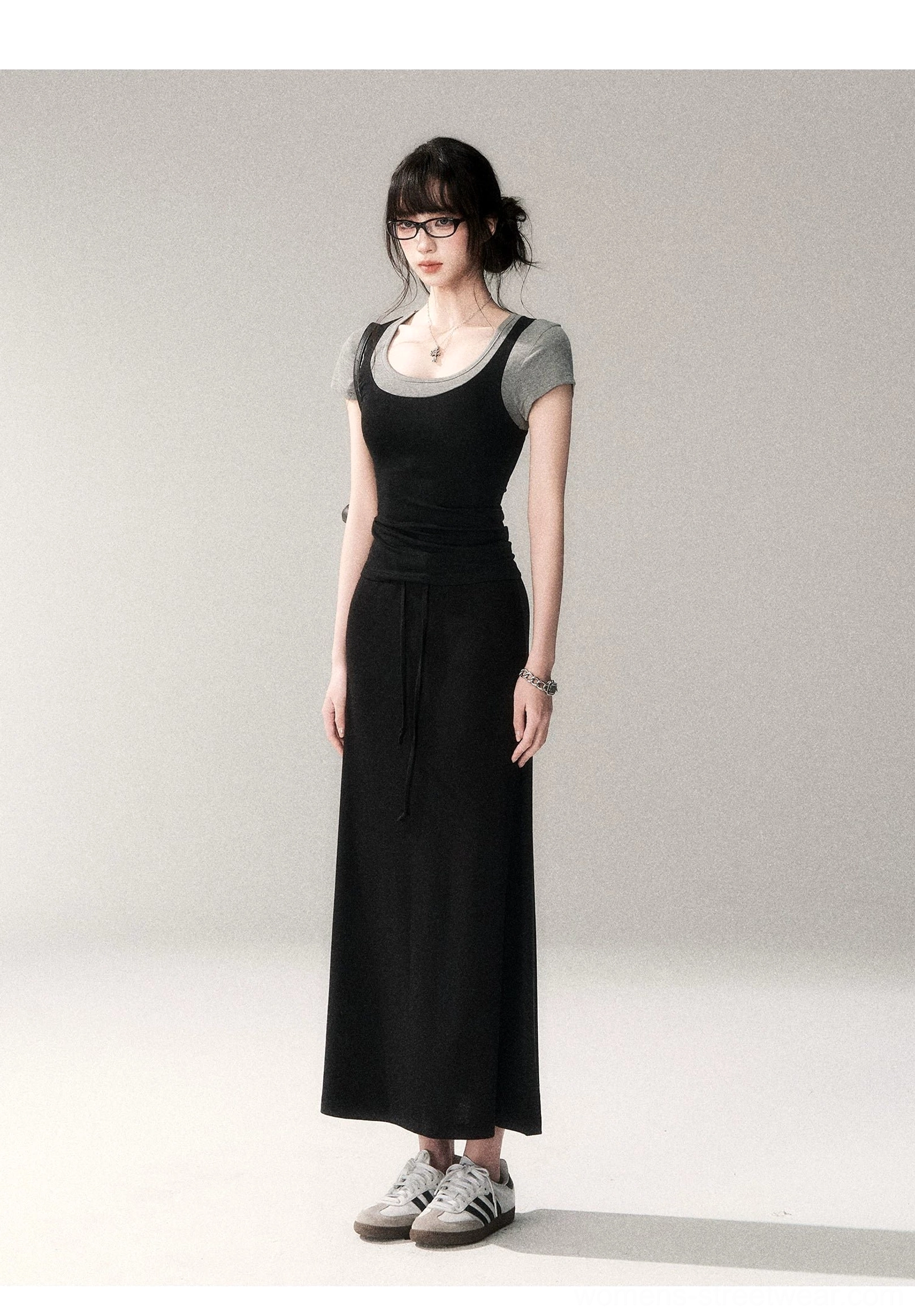 Front three-quarter view of a gray trim scoop neck Korean fashion top layered beneath a black flowy maxi dress and styled with casual sneakers
