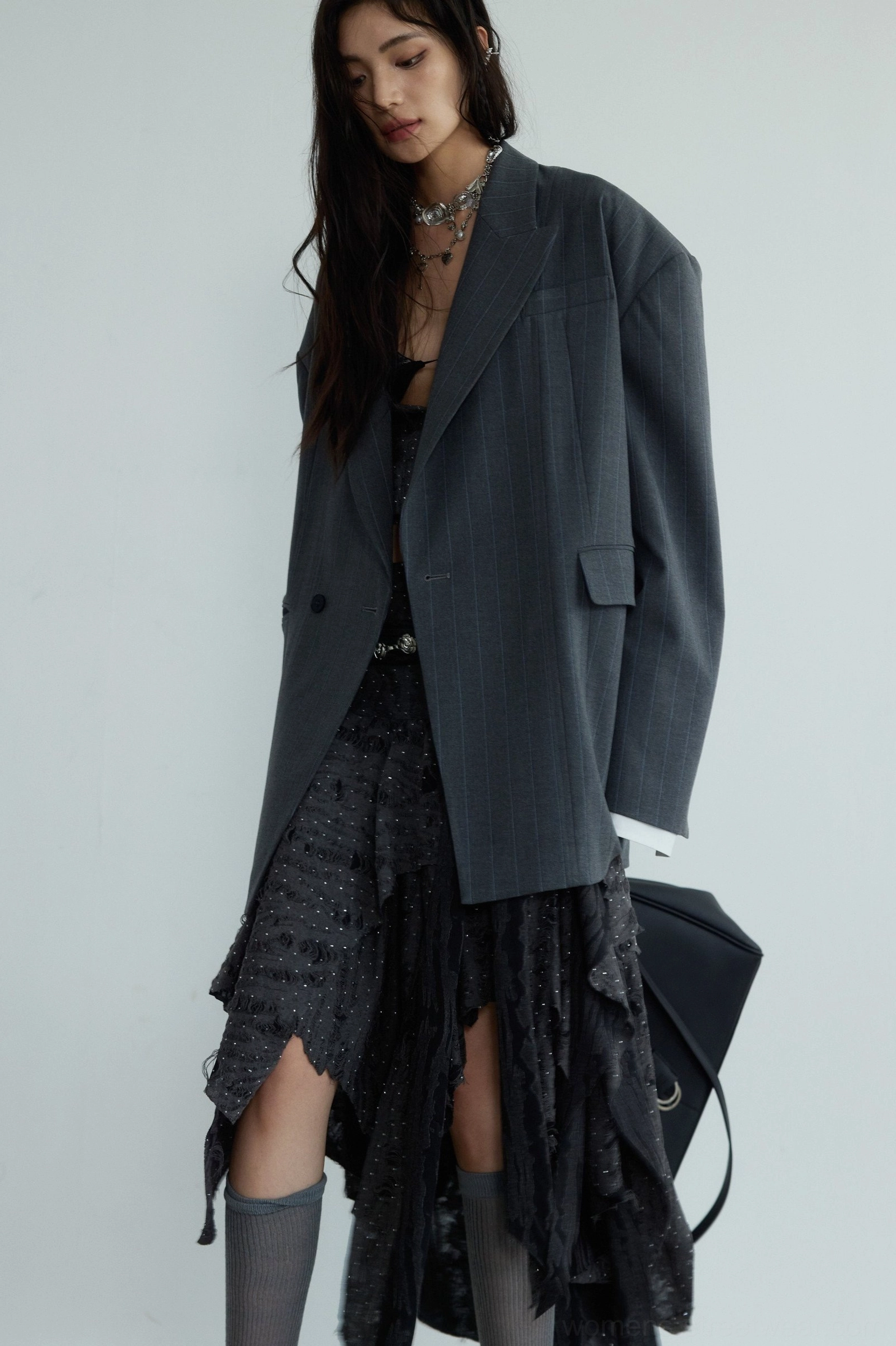Gray unisex oversized striped blazer styled with a dark ruffled skirt neck chain and black tote bag in avant-garde streetwear fashion
